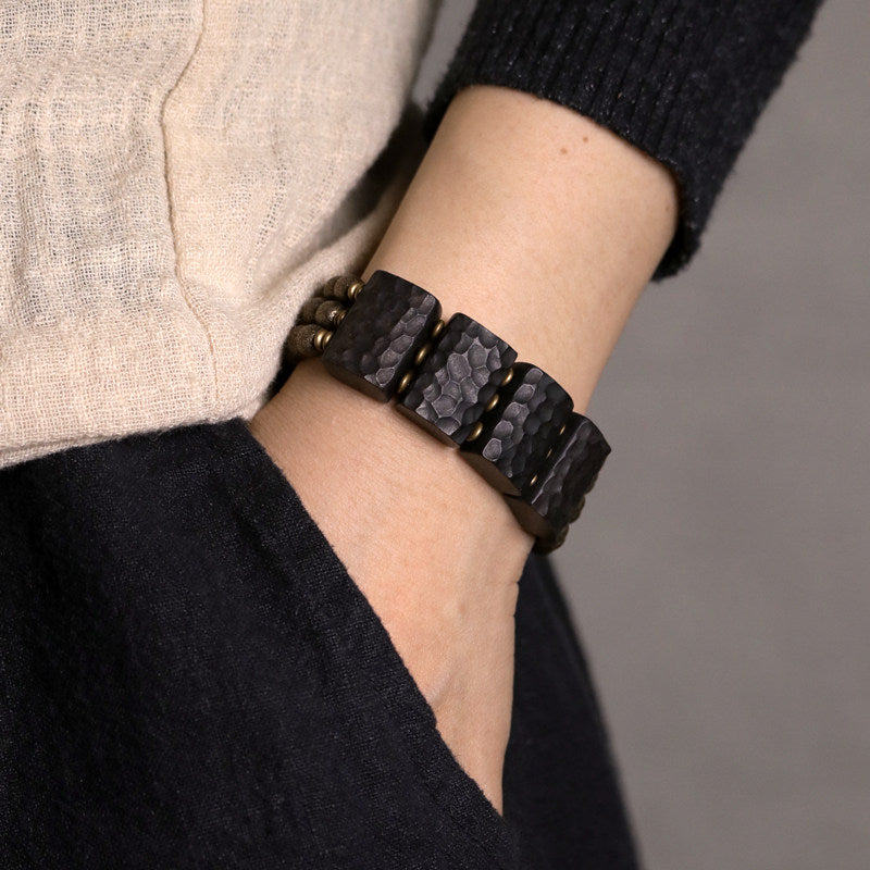 Close-up of Serene Lucky architectural bracelet featuring hand-carved Ebony wood slabs and textured antiqued brass beads on a dark background.