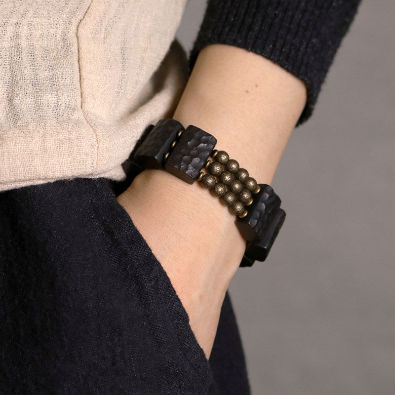 Close-up of Serene Lucky architectural bracelet featuring hand-carved Ebony wood slabs and textured antiqued brass beads on a dark background.