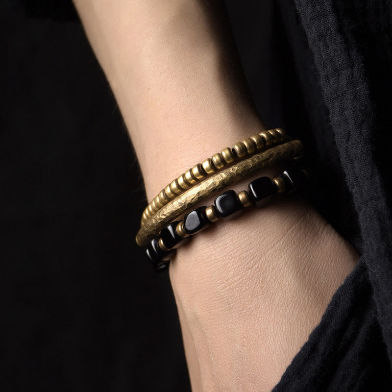 Close-up of Serene Lucky's Night Rhythm bracelet on wrist, featuring square-cut black obsidian beads and multiple antiqued brass spikes.