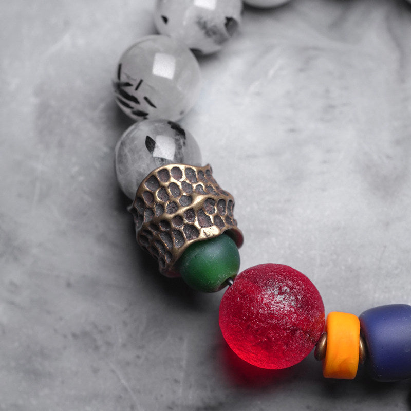 Detailed view of an antique brass hammered metal spacer and a spiral sun pendant on a handmade colorful gemstone bracelet.