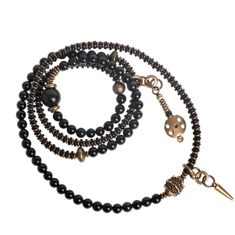 A multi-strand wrap bracelet made of high-polish black onyx beads, textured antique brass spacers, and a vintage spike charm on a white background.