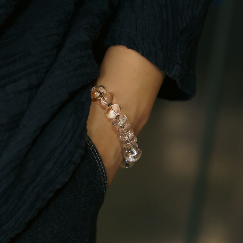 Close-up of a person wearing a clear, translucent beaded bracelet with unique handcrafted texture, styled with a dark navy textured linen shirt.