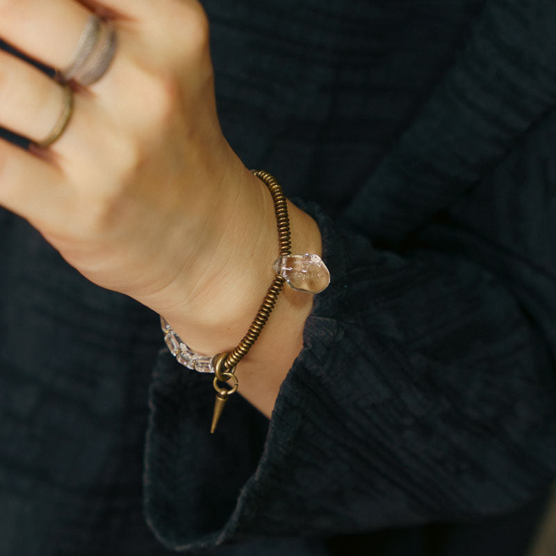 Lifestyle shot showing the clear quartz and brass energy bracelet worn on a wrist with dark linen clothing.