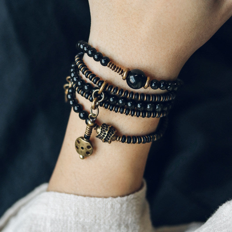 Detailed wrist shot of a handcrafted black beaded bracelet stack with an antique brass medallion charm and textured metal spacers.