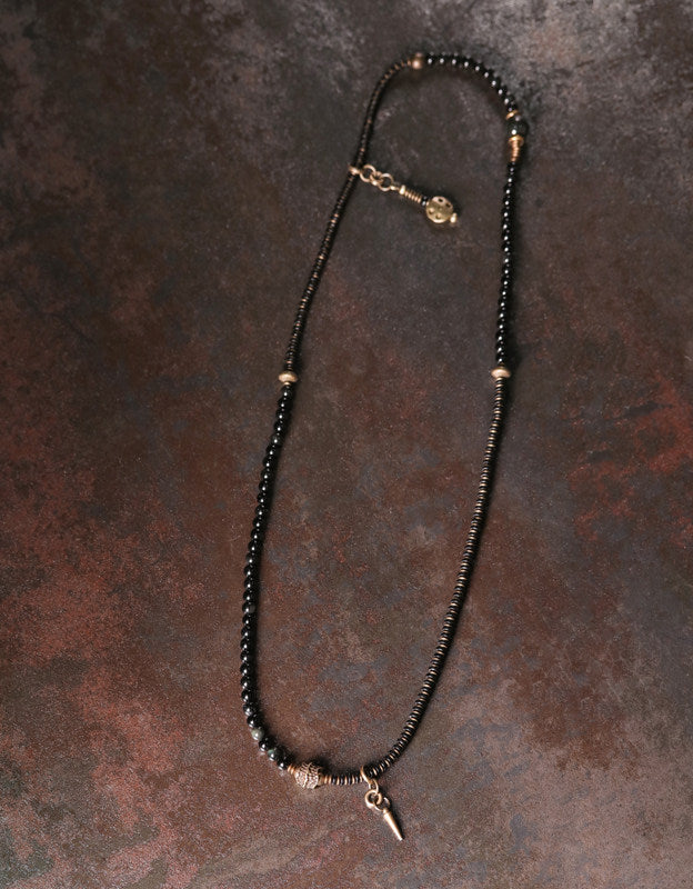 An extra-long handcrafted beaded wrap bracelet laid out to show the alternating black stones, textured brass spacers, and spike details.