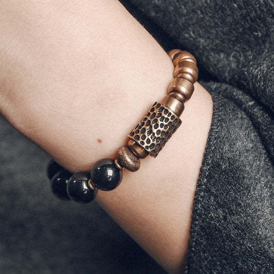 Close-up of a masculine obsidian and brass beaded bracelet worn on a wrist, showcasing its comfortable and grounded aesthetic.