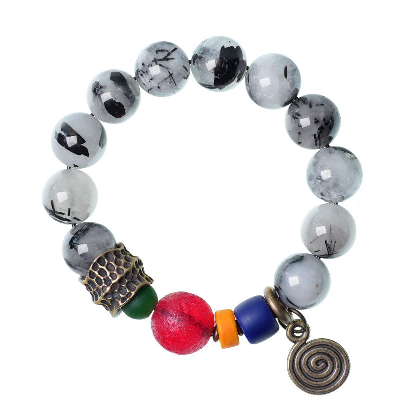Top-down view of a handmade gemstone bracelet featuring black tourmaline quartz and colorful accent beads with a brass spiral pendant, isolated on white.