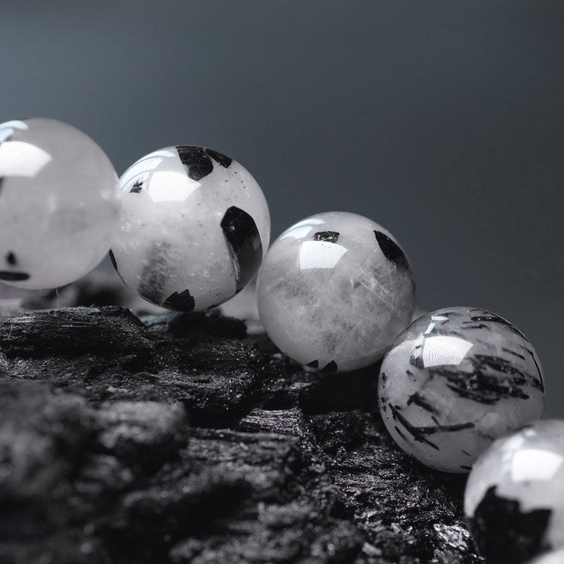 Macro photography of high-quality black rutilated quartz beads, showcasing the unique needle-like tourmaline inclusions and crystalline clarity.