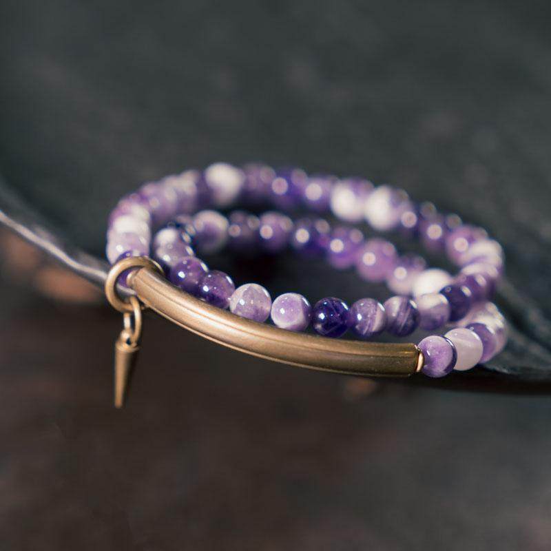 Side-angle macro shot of Serene Lucky multi-wrap bracelet, focusing on the natural inclusions of purple amethyst beads and the smooth matte finish of an antiqued brass tube.