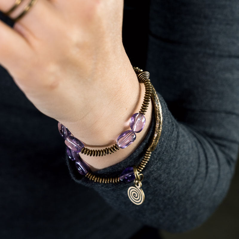 A lifestyle shot of the Serene Lucky Royal Wisdom bracelet, showing the elegant multi-layer wrap design with purple amethyst beads and gold-toned brass tubes on a wrist.