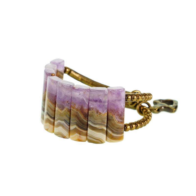High-angle flatlay of Serene Lucky's Royal Wisdom bracelet, featuring parallel rectangular amethyst slabs connected by antiqued brass tubes on a textured dark background.