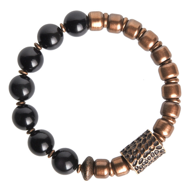 Product studio shot of an obsidian and brass lucky bracelet, featuring a central textured brass cylinder bead for strength and protection.