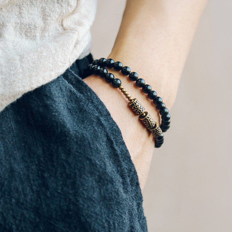 Close-up on wrist showing Serene Lucky's Celestial Weaver bracelet, highlighting the light-catching hollow lattice brass spheres and obsidian wrap.