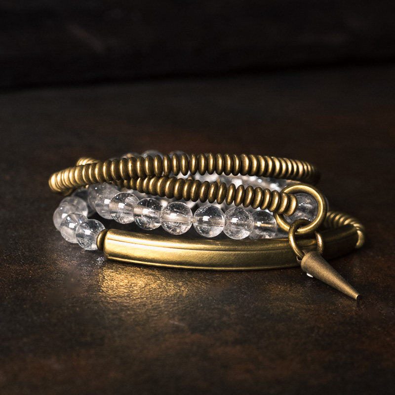 Macro studio shot of Serene Lucky multi-wrap bracelet, showing clear quartz beads, a brass spike charm, and a crystal-encrusted rondelle spacer on a clean white background.
