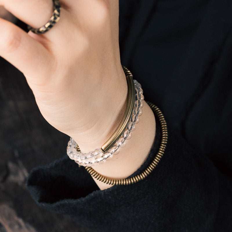 Top-down view of the Serene Lucky multi-wrap bracelet, showcasing layers of clear quartz beads separated by long polished brass tubes for a modern minimalist look.