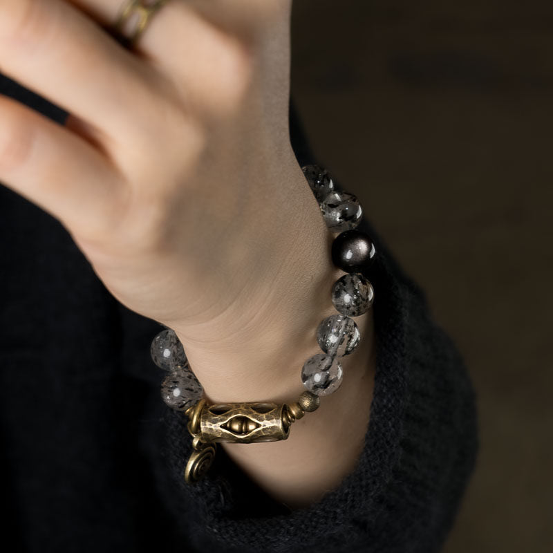 Macro detail of Serene Lucky Cosmic Shield bracelet, showcasing the intricate floral etched brass tube, spiral charm, and the crystalline texture of Black Mica Quartz beads.