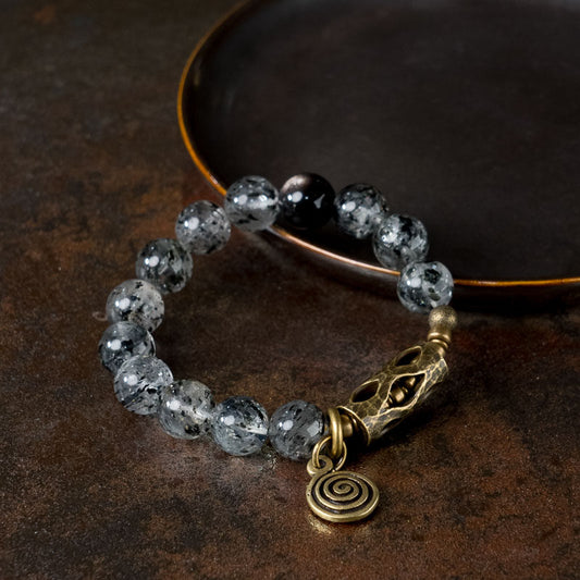 Serene Lucky Cosmic Shield bracelet featuring natural Silver Sheen Obsidian and Black Mica Quartz beads with a decorative floral brass tube and spiral charm.