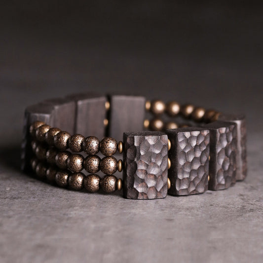 Close-up of Serene Lucky architectural bracelet featuring hand-carved Ebony wood slabs and textured antiqued brass beads on a dark background.
