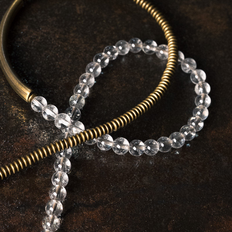 Macro detail of Serene Lucky bracelet showing faceted clear quartz beads and the unique coiled texture of the antiqued brass spacers with technical annotations.
