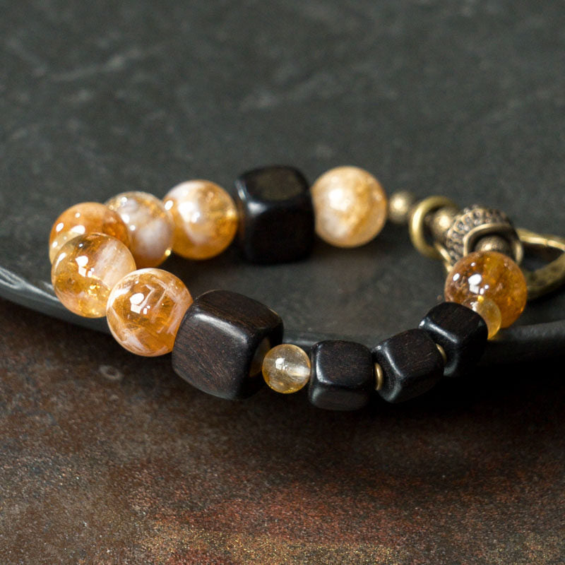 A lifestyle shot of the Serene Lucky Golden Clarity bracelet worn on a wrist, featuring dark ebony wood cubes and glowing yellow citrine beads for a zen-inspired aesthetic.