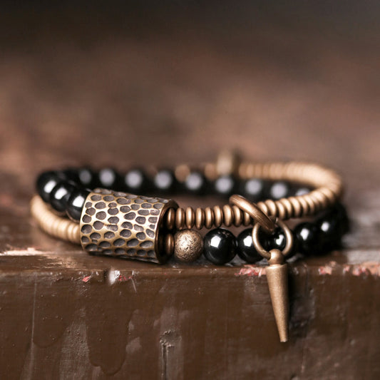Close-up of Serene Lucky's Midnight Fortress bracelet on a rustic wooden surface, highlighting hammered brass cylinders and glossy black obsidian beads.