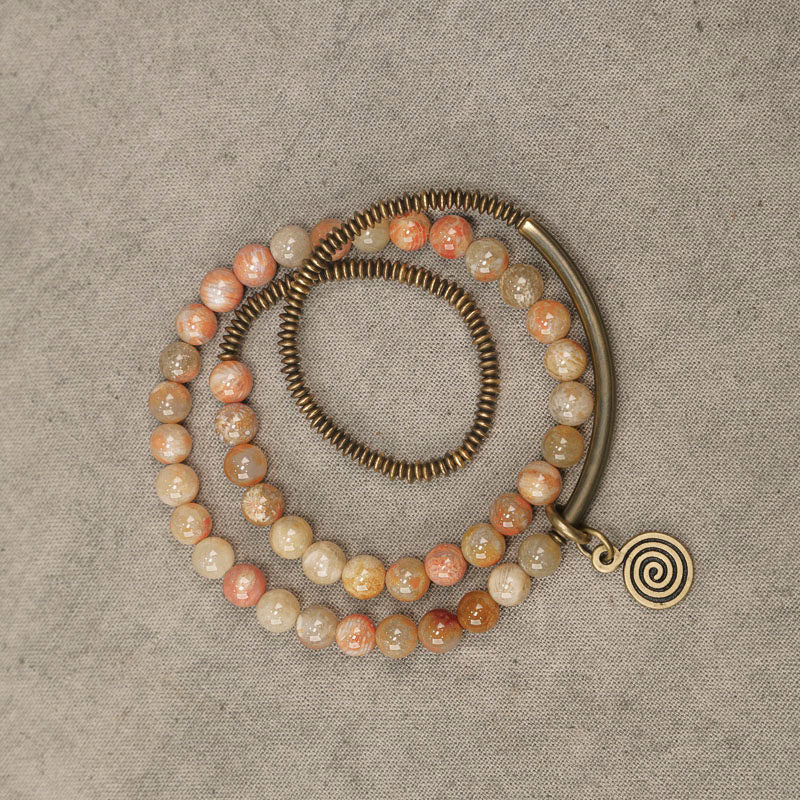 Full view of the Serene Lucky multi-wrap bracelet showcasing the alternating layers of coral stone beads and antiqued brass architectural elements.