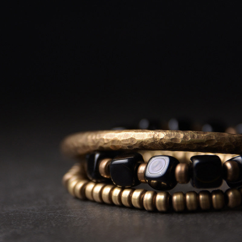 Macro detail of Serene Lucky's Night Rhythm bracelet, showing the contrast between square black obsidian beads and hammered antiqued brass hardware.