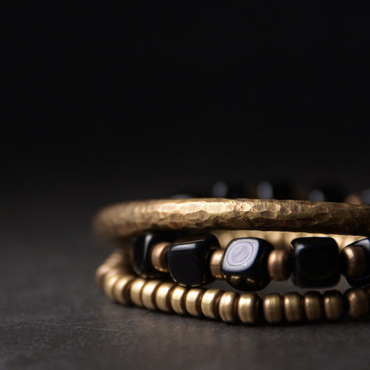 Macro detail of Serene Lucky's Night Rhythm bracelet, showing the contrast between square black obsidian beads and hammered antiqued brass hardware.