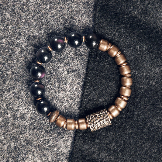 Handcrafted Serene Lucky bracelet featuring deep black obsidian stones and vintage-style brass beads on a textured grey background.