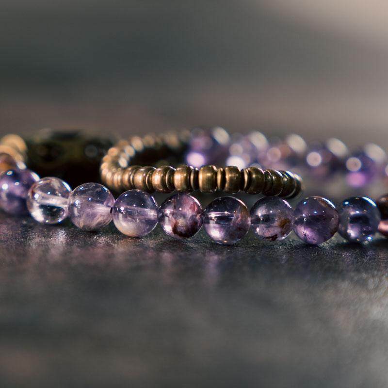 Close-up detail of Serene Lucky multi-wrap bracelet featuring natural purple phantom quartz beads and long curved antiqued brass tubes, showing the exquisite handcrafted texture.