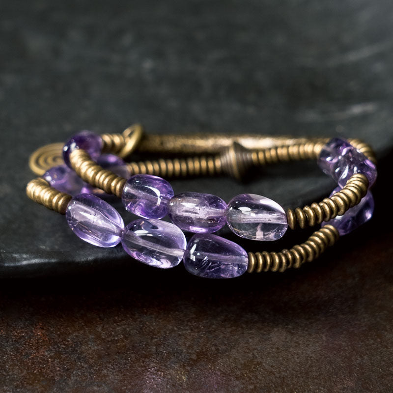 Macro shot of the Serene Lucky Royal Wisdom bracelet, showing a translucent purple amethyst bead nested in a matte gold-toned brass architectural element.