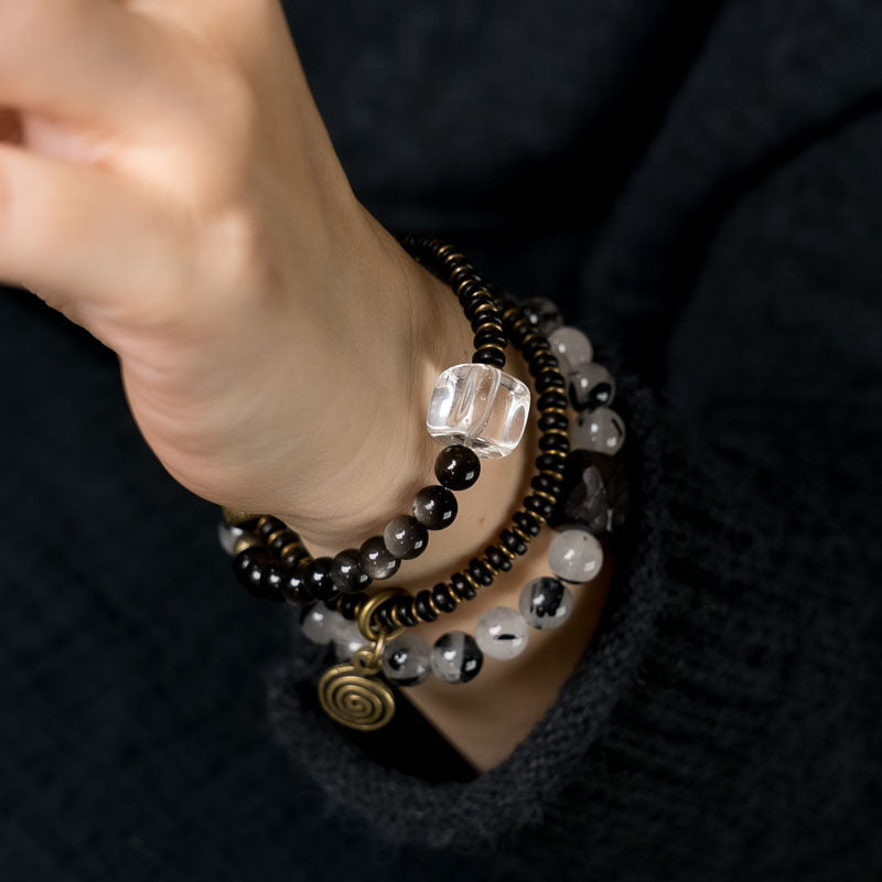 Serene Lucky "Shadow & Light" multi-layer wrap bracelet featuring natural Ebony wood, shimmering Silver Sheen Obsidian, and Clear Quartz with architectural antiqued brass accents.