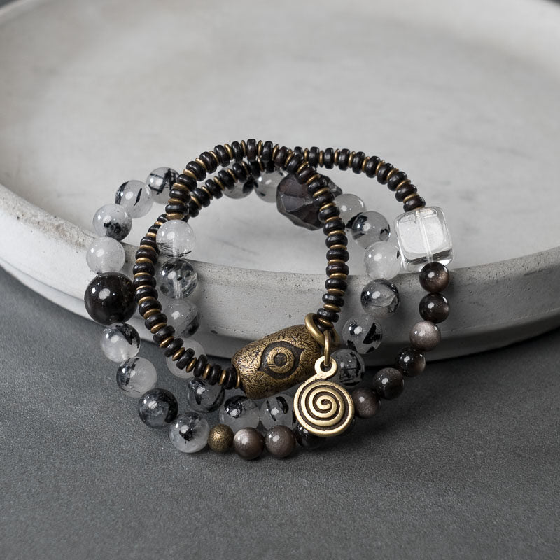 Serene Lucky "Shadow & Light" multi-layer wrap bracelet featuring natural Ebony wood, shimmering Silver Sheen Obsidian, and Clear Quartz with architectural antiqued brass accents.
