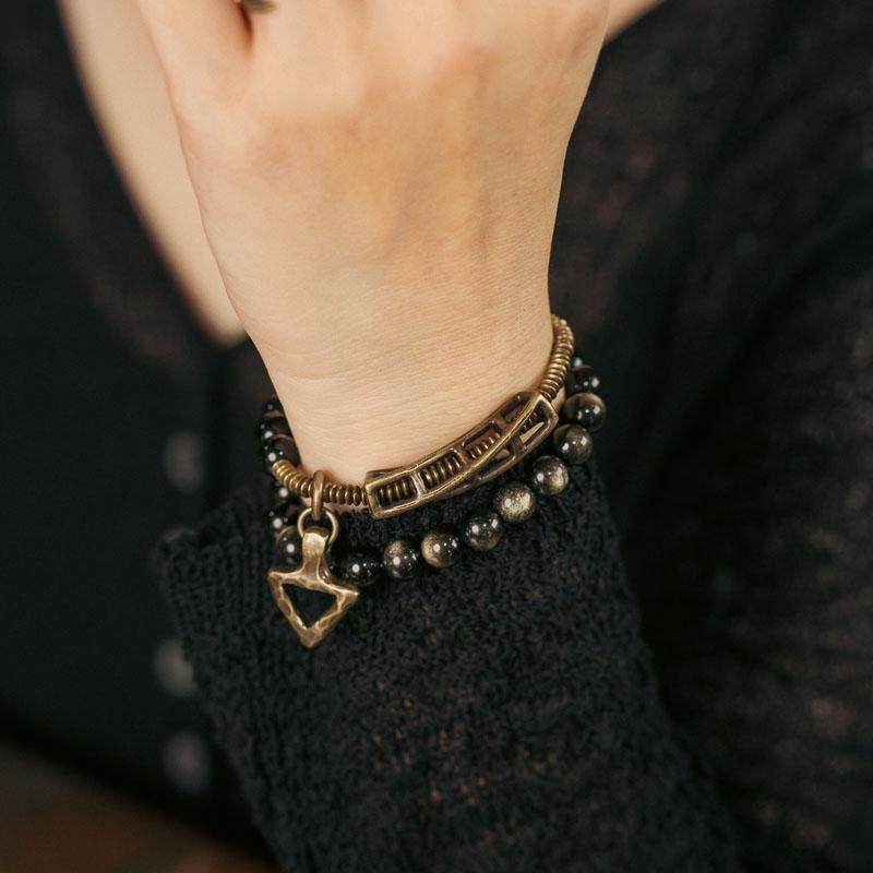 A model wearing the Serene Lucky Solar Gears wrap bracelet, demonstrating the layered look of golden sheen obsidian and industrial brass gears on the wrist.