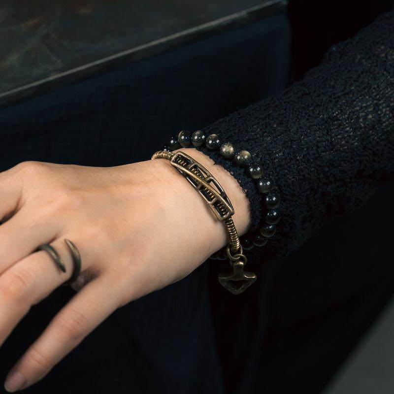 A close-up of the Serene Lucky Solar Gears bracelet wrapped around a wrist, showcasing the contrast between the golden sheen obsidian and industrial gear brass beads.