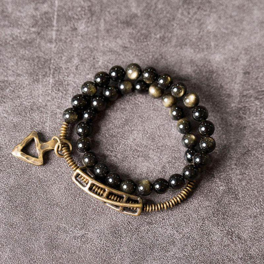 A cinematic shot of Serene Lucky's Solar Gears bracelet on a grey slate surface, highlighting the shimmering golden sheen obsidian and brass gear accents.