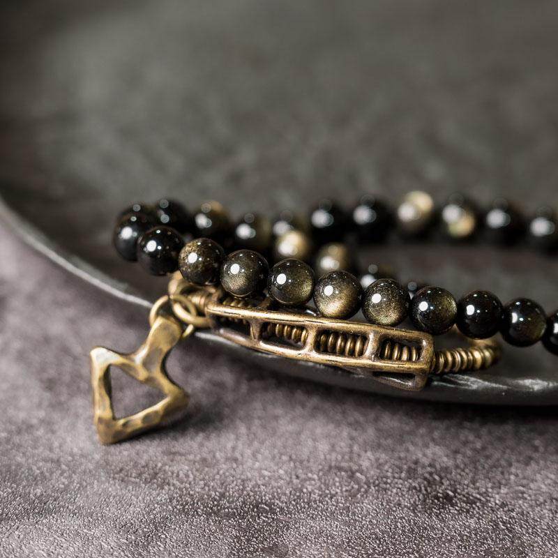 Macro view of Serene Lucky's Solar Gears bracelet, showing the shimmering gold sand effect inside obsidian beads and the intricate gear texture on brass accents.