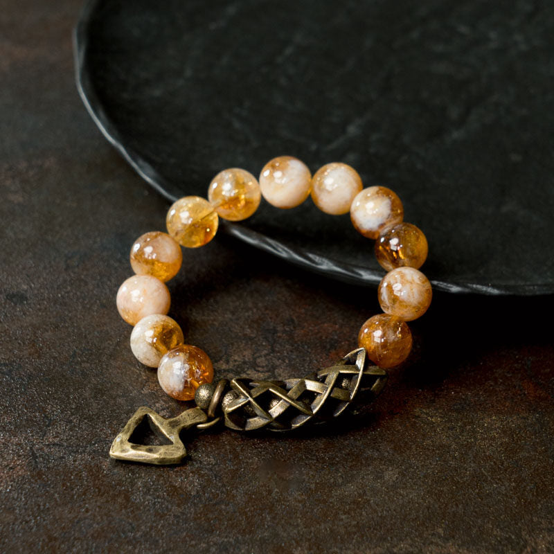 A close-up of a person wearing the Serene Lucky Solar Path bracelet, highlighting the handcrafted brass triangle charm and woven metal tube against faceted citrine beads.