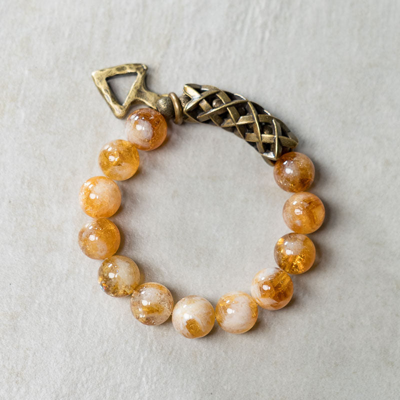 Close-up of the Serene Lucky Solar Path bracelet on a wrist, featuring a handcrafted brass spiral disc charm and woven metal tube with translucent yellow citrine beads.