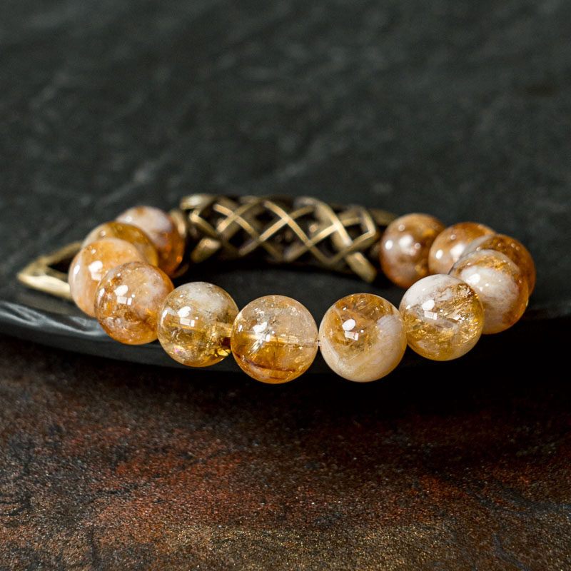 A high-contrast lifestyle shot of the Serene Lucky bracelet, featuring translucent yellow citrine beads interlaced with intricately carved floral filigree brass spacers on a wrist.