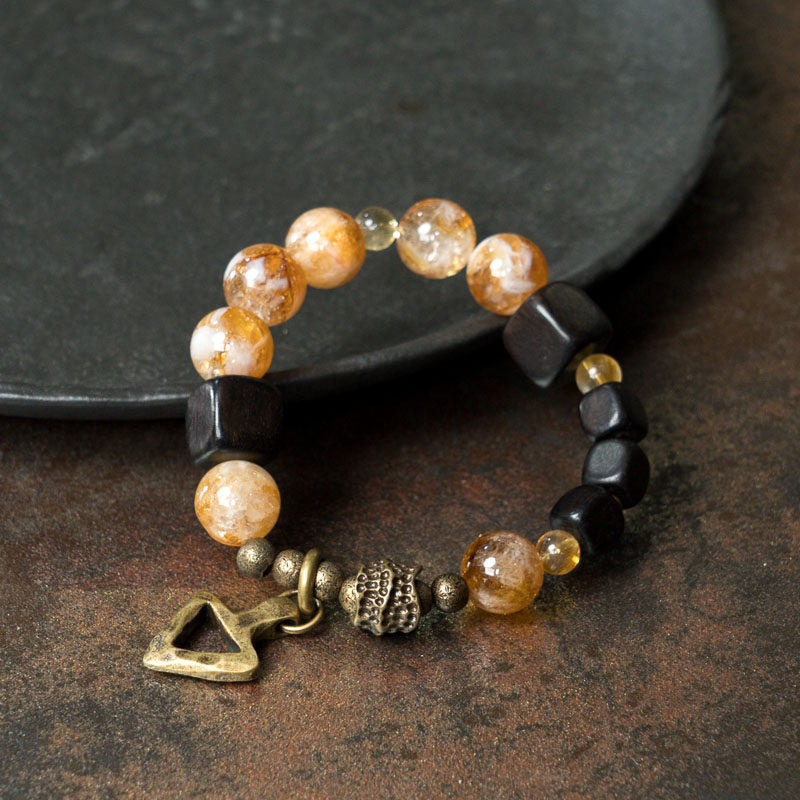 Side view of Serene Lucky Golden Clarity bracelet, showcasing the contrast between square ebony wood beads, round yellow citrine, and a curved brass tube with floral etching.