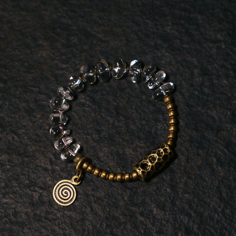 Top-down view of a handmade bracelet combining clear faceted beads and rustic brass components with a unique spiral pendant.