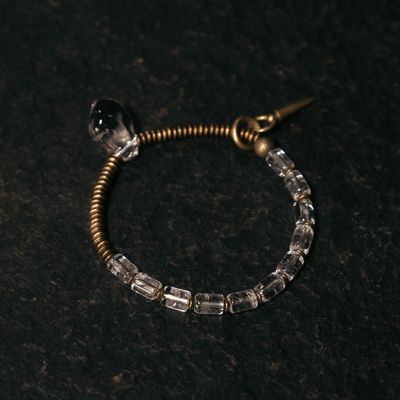 Top down view of a vintage brass coiled bracelet with clear quartz beads on a dark textured background.