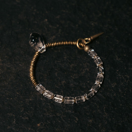 Top down view of a vintage brass coiled bracelet with clear quartz beads on a dark textured background.