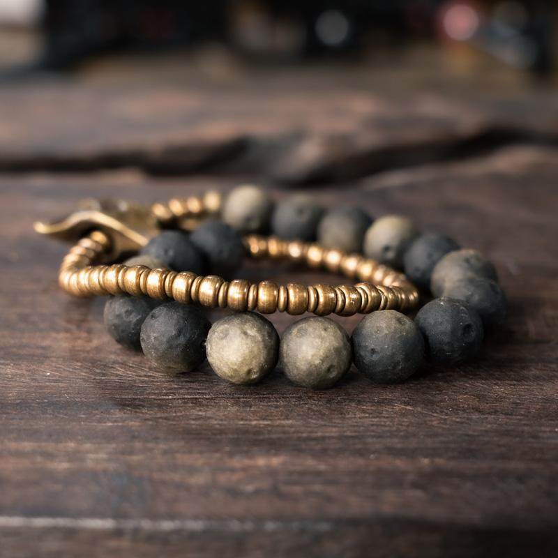 Side view of a Western-style bracelet stack combining textured brass rondelle beads and black volcanic rock spheres for a rugged look.
